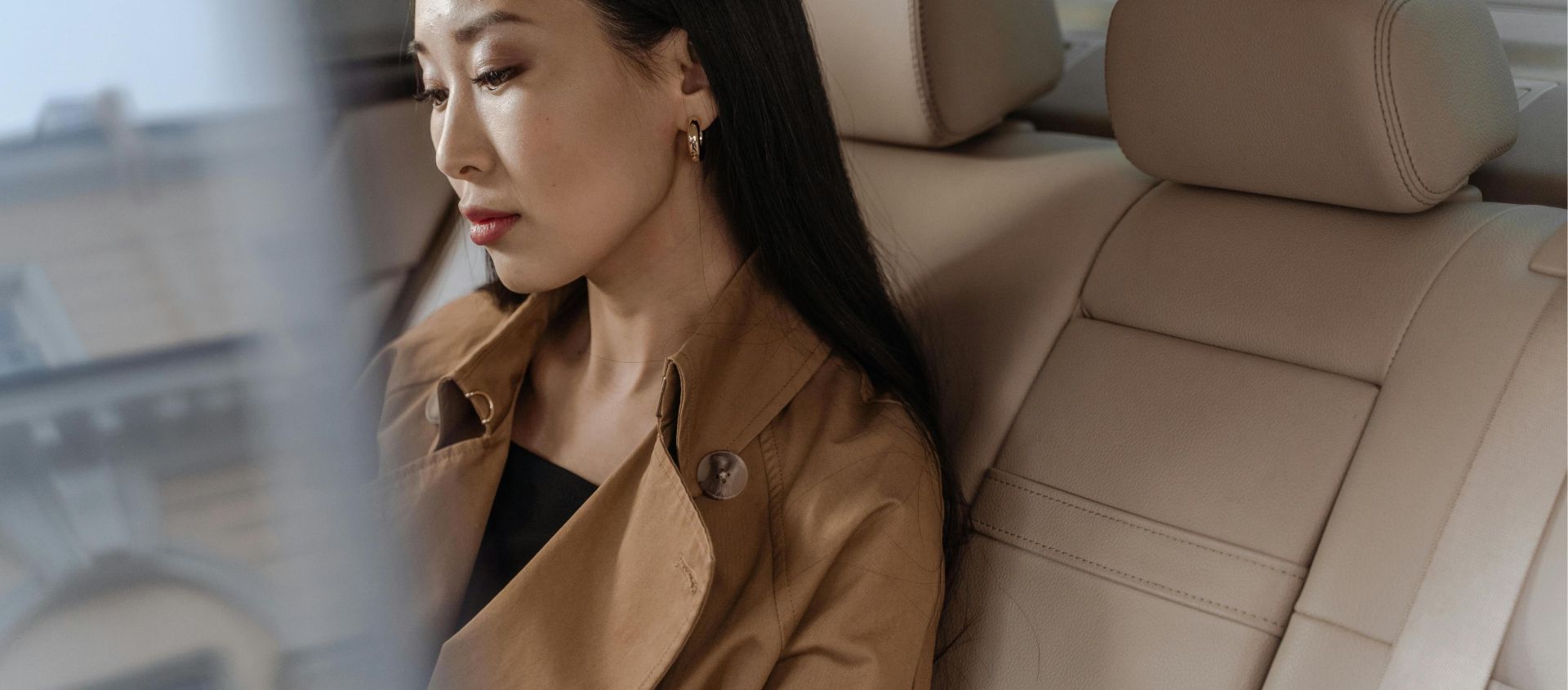 An elegant Asian woman sits thoughtfully in a luxurious car interior.