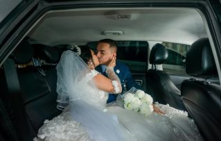 Happy newlywed couple sharing a kiss in a car with white bouquet after wedding in Santo Domingo.